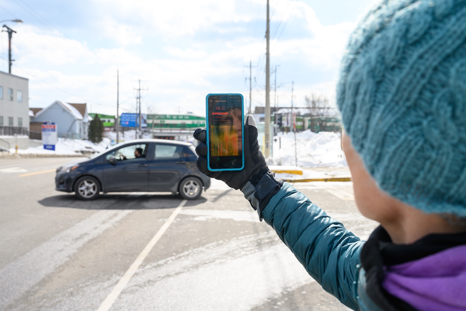 Person holding a smartphone up in the street, with a card in the background. The phone is showing a noise measuring app